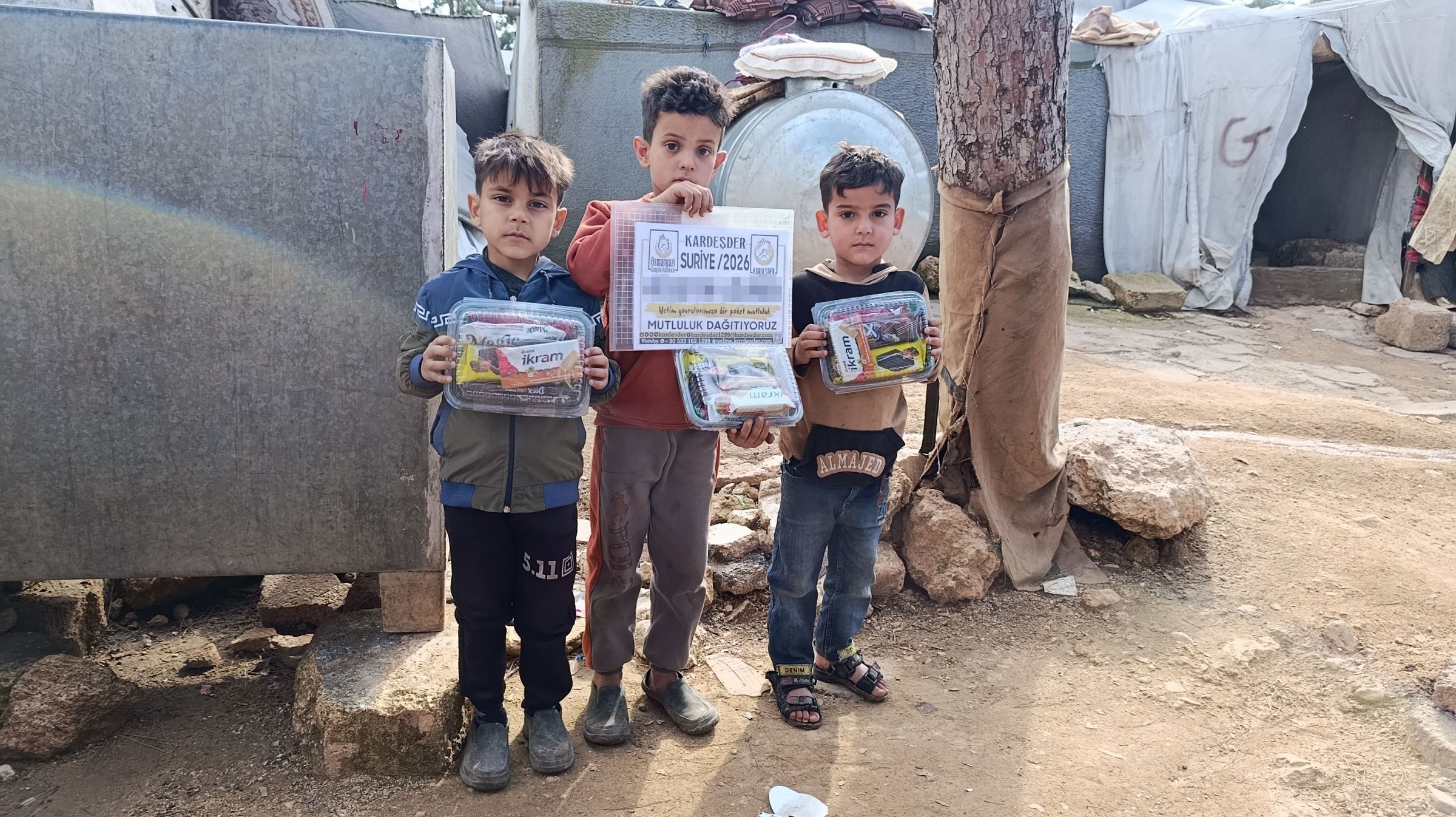 Suriye’deki bir kampta, ellerinde ekmek poşetleriyle duran çocuklar